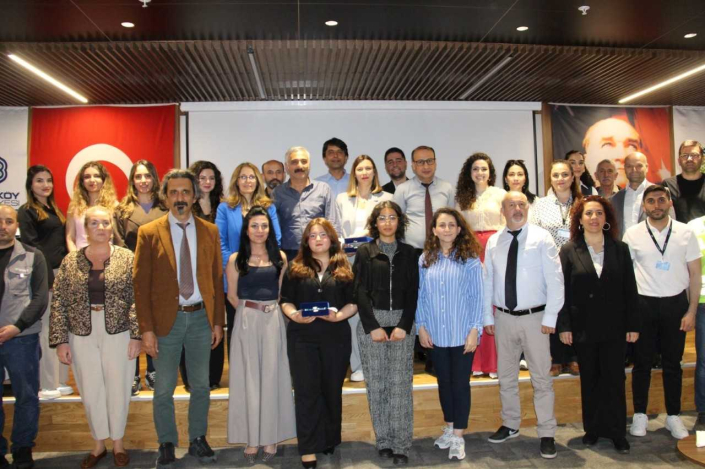 Bir konferans salonunda bir etkinlik sonrası çekilmiş, Türk bayrağı ve Atatürk portresi önünde duran çok sayıda katılımcıdan oluşan grup fotoğrafı.