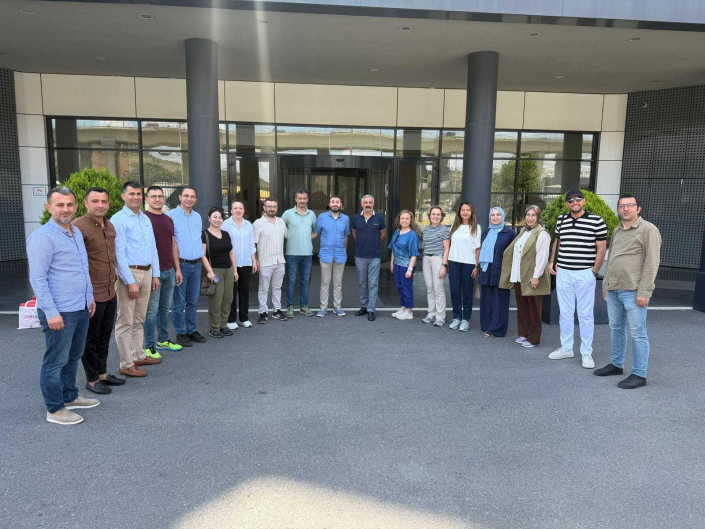 Bir binanın girişinde, açık havada yan yana dizilerek kameraya poz veren kadın ve erkeklerden oluşan kalabalık bir katılımcı grubu.