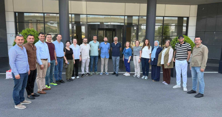 Bir binanın girişinde, açık havada yan yana dizilerek kameraya poz veren kadın ve erkeklerden oluşan kalabalık bir katılımcı grubu.