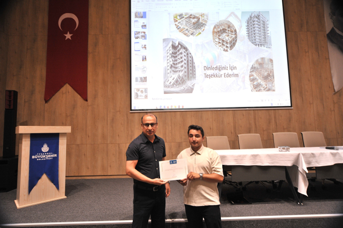 Bir seminer salonunda, arkalarında 'Dinlediğiniz İçin Teşekkür Ederim' yazılı sunum ekranı önünde yan yana durarak sertifika tutan iki erkek.