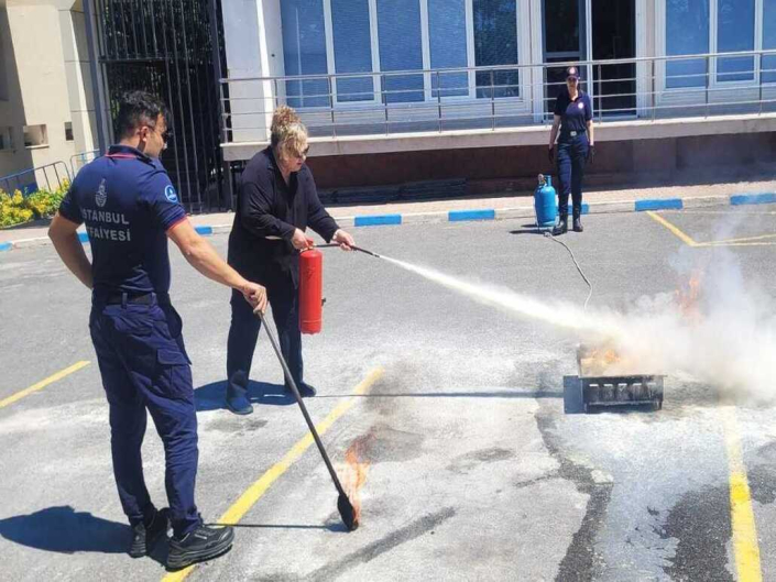 Yangın eğitimi sırasında, itfaiye personelinin rehberliğinde yangın söndürme tüpüyle yerdeki ateşe müdahale eden bir kadın.