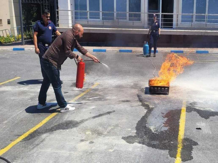 Yangın eğitimi sırasında, bir kişinin kırmızı yangın söndürme tüpüyle yerdeki yanan kutuya müdahale ettiği an.