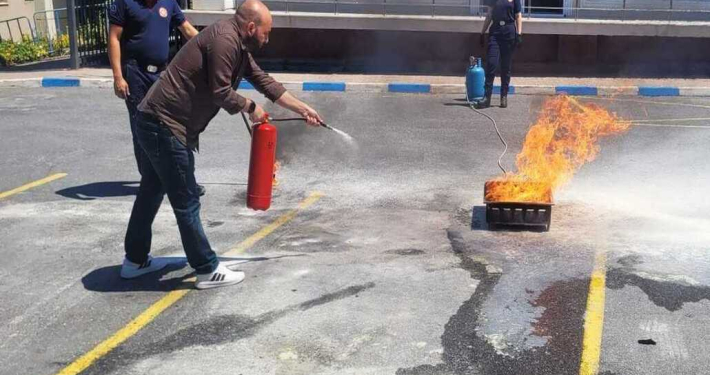 Yangın eğitimi sırasında, bir kişinin kırmızı yangın söndürme tüpüyle yerdeki yanan kutuya müdahale ettiği an.