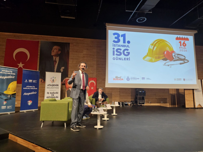 Fotoğrafta, bir sahnede sunum yapan takım elbiseli bir konuşmacı ve arka plandaki projeksiyon ekranında "31. İstanbul İSG Günleri" başlığı yer almaktadır.
