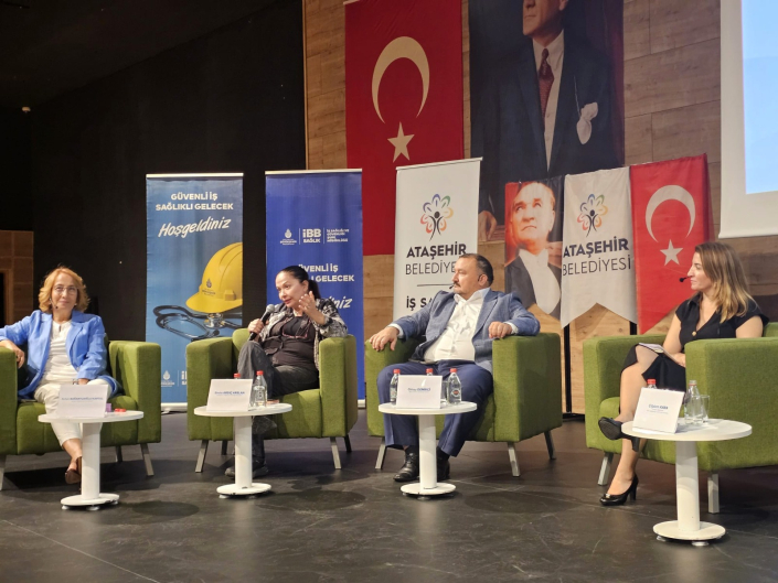 Fotoğrafta, bir sahnede yeşil tekli koltuklarda yan yana oturan ve panel gerçekleştiren dört konuşmacı yer almaktadır.