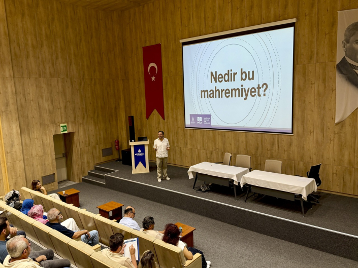 Türk bayrağı ve Atatürk portresinin asılı olduğu ahşap panelli bir salonda, sahnedeki konuşmacının arkasındaki perdede Türkçe "Nedir bu mahremiyet?" yazılı bir slayt gösteriliyor.